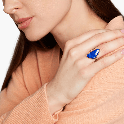 dark blue statement ring slightly triangle-shaped; model wears light peach sweater and has her hand on her shoulder to display the ring