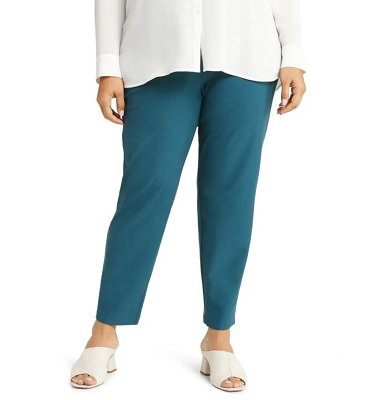 A woman wearing a white blouse, teal pants, and white sandals