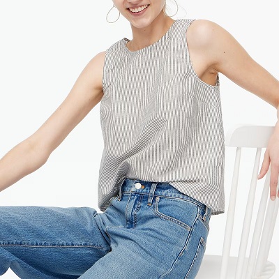 A woman sitting on a white wooden chair, wearing a striped linen tank top and blue jeans