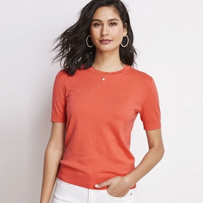 A woman wearing an orange short-sleeved sweater and white pants