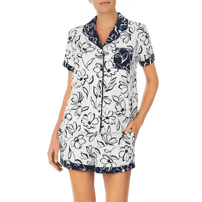 woman wears white and black PJs with a floral print; the PJs have a reversed print on the collar, pocket, and cuffs of the shorts so there are white flowers on a black/navy background