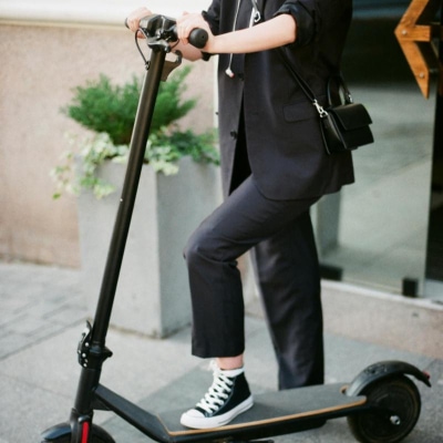 carefree woman wears a black suit and sneakers and is about to ride a scooter