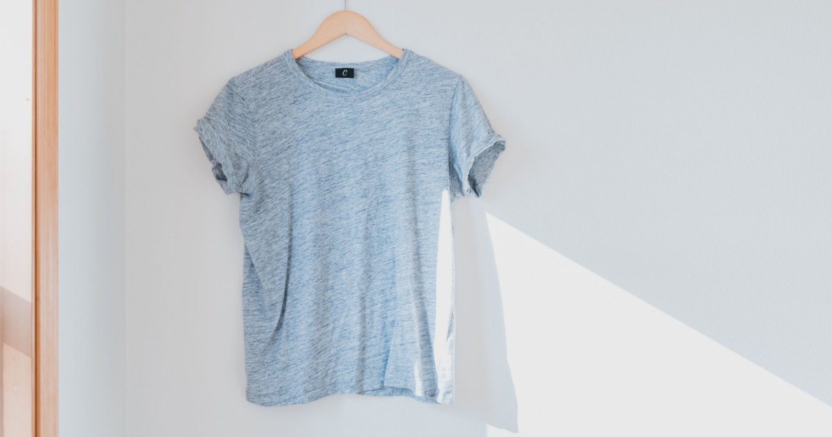 A light blue T-shirt (possibly worn but not dirty!) hanging on a wooden hanger against a white wall