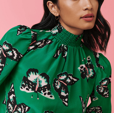 woman wears green blouse with a ruched mock neck and slight puff sleeves; the shirt