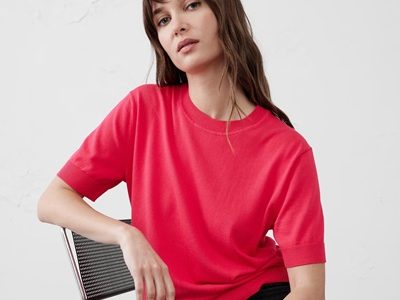 A woman sitting on a chair, wearing black pants and a coral short-sleeved sweater