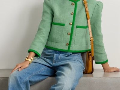 A woman sitting down wearing a green Lady Jacket, jeans, and carrying a brown handbag
