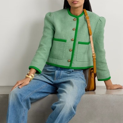 A woman sitting down wearing a green Lady Jacket, jeans, and carrying a brown handbag