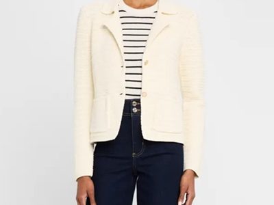 A woman wearing a cream blazer, striped top, and dark blue jeans