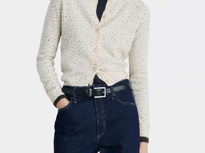 A woman wearing a white polka dots cardigan top and dark blue denim pants with black belt