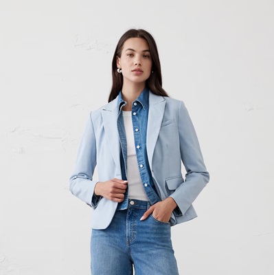 A woman wearing a denim shirt, jeans, white top, and light blue blazer