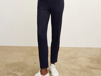 A woman standing on a concrete floor wearing a white top, navy pants, and white sneakers