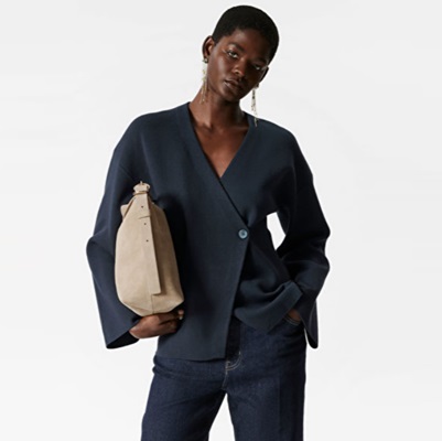 A woman wearing dark blue jeans, a navy blazer, and carrying a tan handbag