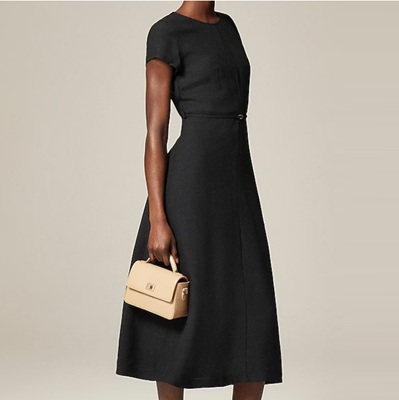 A woman wearing a midi black dress with black heels and a cream-colored handbag