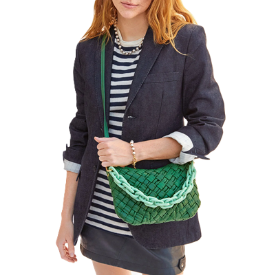 woman carries green bag with woven details and mint green chain strap; she has reddish hair and is wearing a blue blazer, a striped tee, and a leather miniskirt