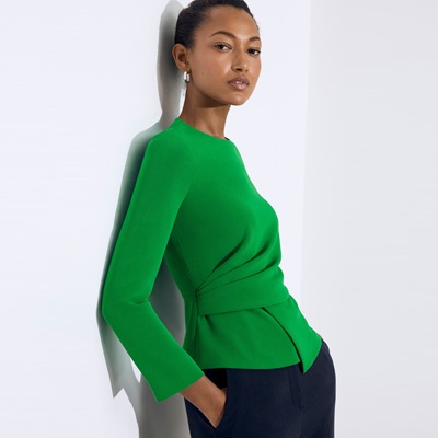 A woman wearing a bright green top and navy pants, leaning against a wall