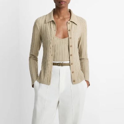 A woman wearing a light brown top with a long sleeve cardigan and white trouser pants with belt
