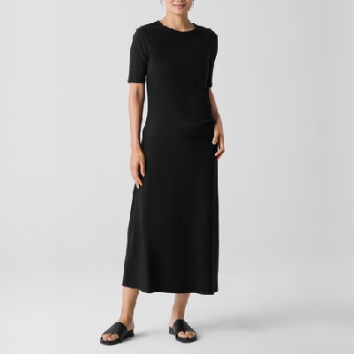 A woman wearing a black crew neck top and black skirt with black sandals