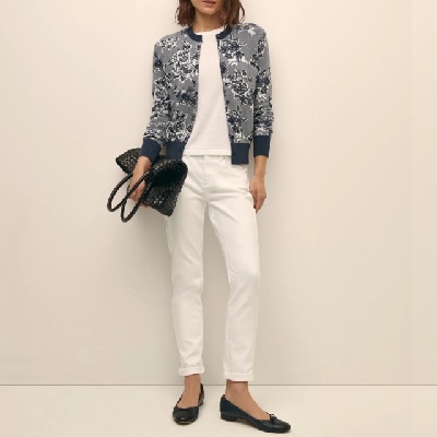 A woman wearing a white inner shirt with a blue floral printed cardigan with white pants and black doll shoes with black hand bag