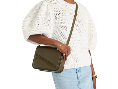 Black woman carries olive structured bag across her body; she is wearing a white puffy-sleeved sweater