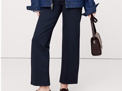 A woman wearing navy ponte pants, brown loafers, a white top, and blue denim jacket, and holding a brown croc bag