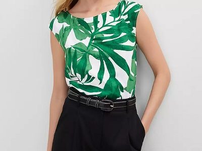 A woman wearing a white green floral printed top and black pants with black belt