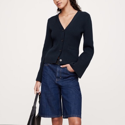 A woman wearing a dark blue long sleeve cardigan top and denim short with black bag