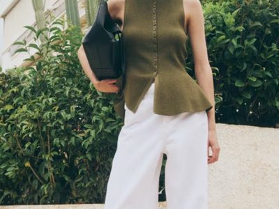 A woman wearing a green sleeveless top and white trouser pants with black hand bag