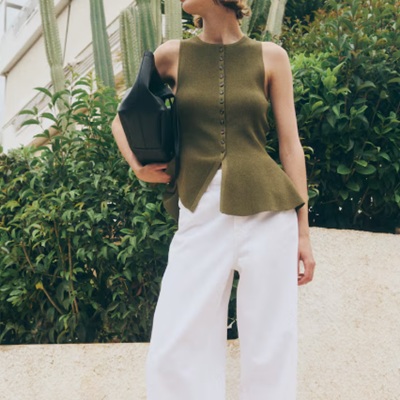 A woman wearing a green sleeveless top and white trouser pants with black hand bag