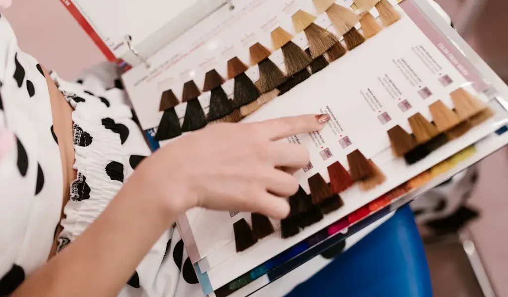 Woman selecting hair Best Hair Colors for Fall and Winter 2025 color samples in a salon, showcasing shades of brown and blonde.