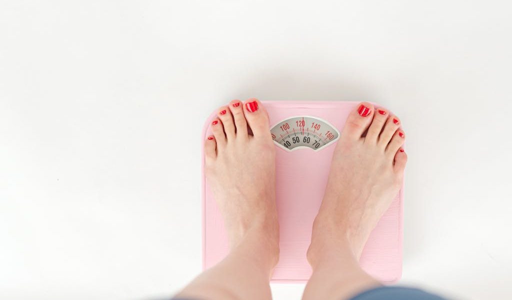 Top view of crop anonymous barefoot female measuring weight on scales on white background