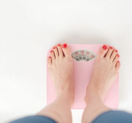 Top view of crop anonymous barefoot female measuring weight on scales on white background