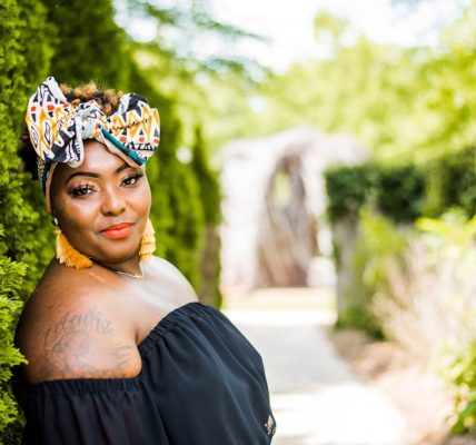 Confident woman wearing headscarf and tassel earrings in a vibrant green outdoor setting.