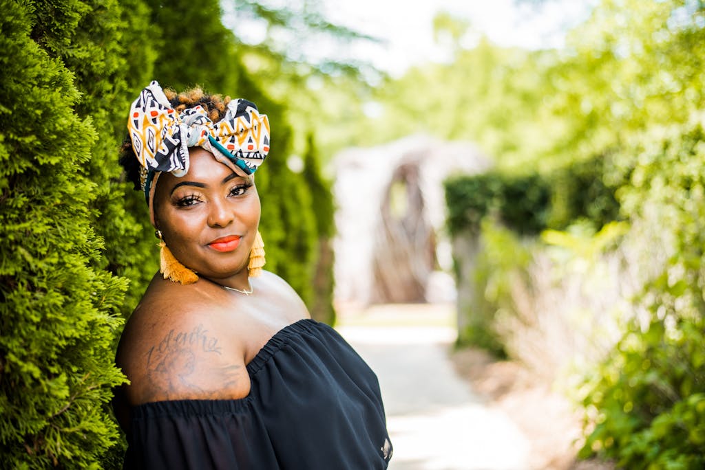 Confident woman wearing headscarf and tassel earrings in a vibrant green outdoor setting.