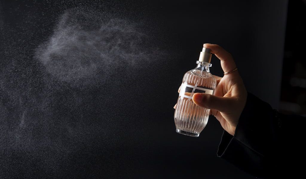 A hand elegantly spritzing perfume from a decorative bottle against a dark background. how perfume notes work