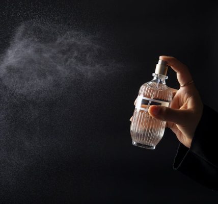 A hand elegantly spritzing perfume from a decorative bottle against a dark background. how perfume notes work