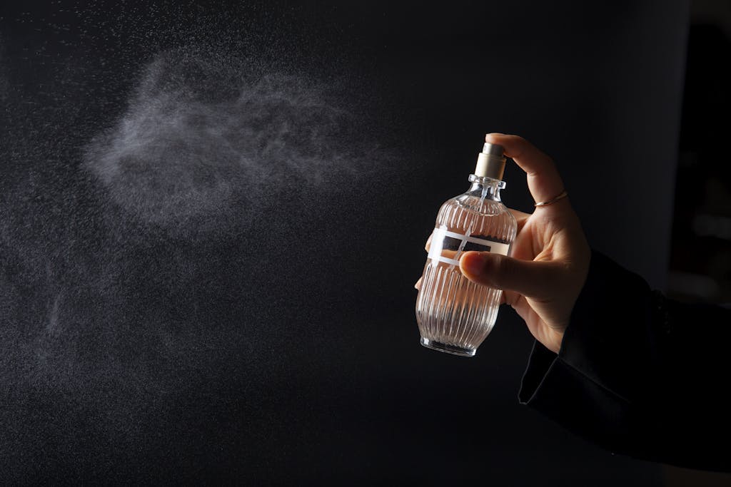 A hand elegantly spritzing perfume from a decorative bottle against a dark background. how perfume notes work