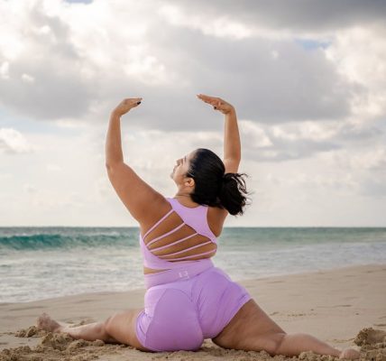 A woman performs yoga on a sandy beach, showcasing strength and flexibility in a serene coastal environment.