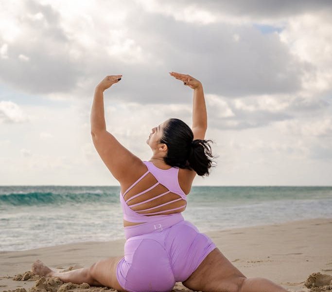 A woman performs yoga on a sandy beach, showcasing strength and flexibility in a serene coastal environment.
