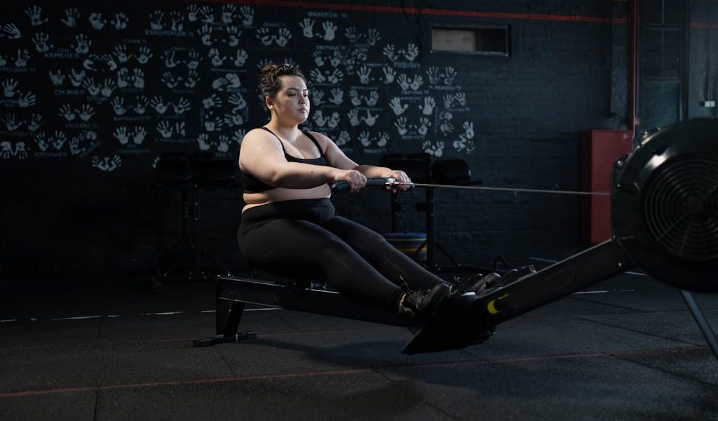 Plus-size woman working out on a rowing machine indoors, embracing fitness and a healthy lifestyle.
