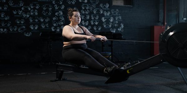 Plus-size woman working out on a rowing machine indoors, embracing fitness and a healthy lifestyle.