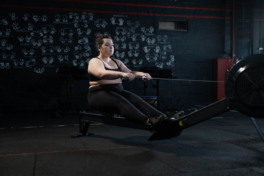 Plus-size woman working out on a rowing machine indoors, embracing fitness and a healthy lifestyle.