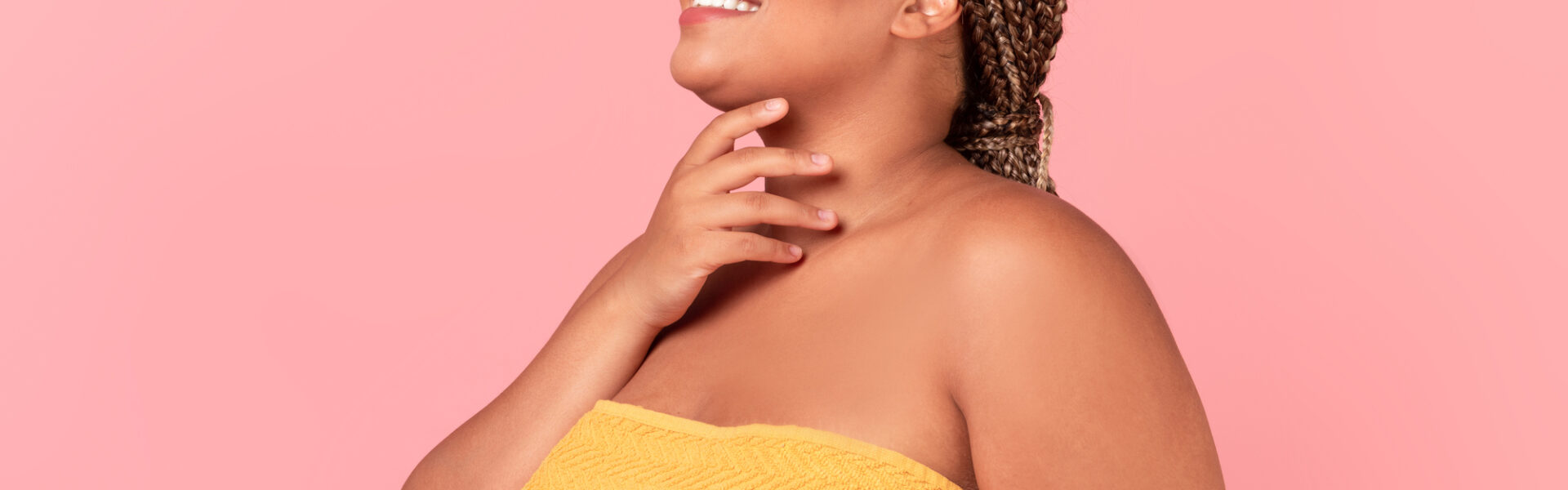 Self love and acceptance concept. Portrait of happy black chubby woman with perfect skin posing wrapped in towel and touching neck, enjoying her natural beauty over pink background