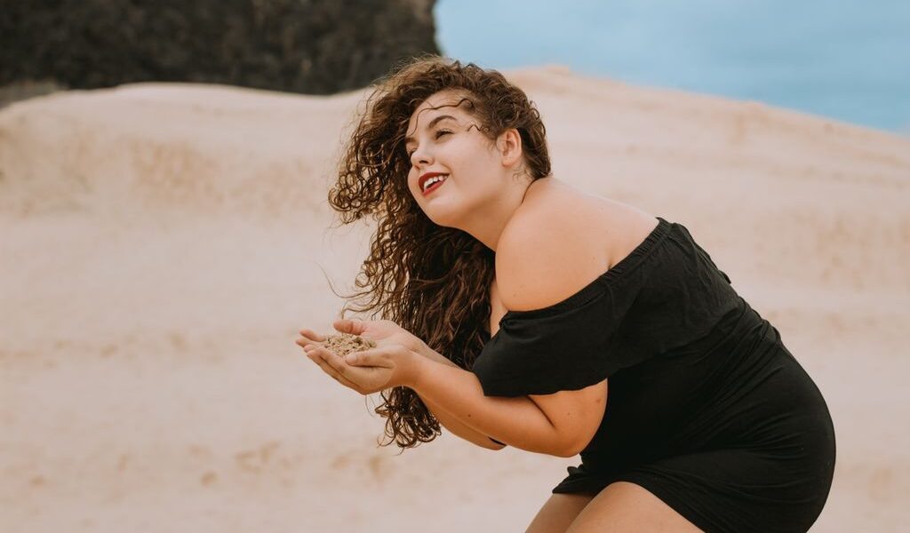 Woman in a black dress at the beach enjoying sand. Perfect for summer and leisure themes.