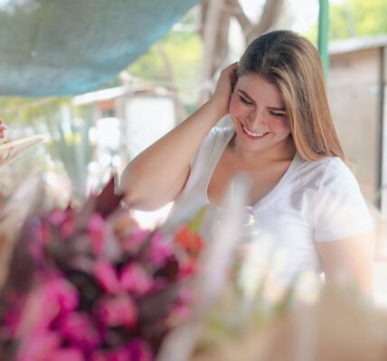 A happy woman in a white t-shirt enjoys browsing vibrant bouquets at a flower market.
