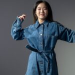 A fashionable woman poses confidently in a denim dress, showcasing modern style.