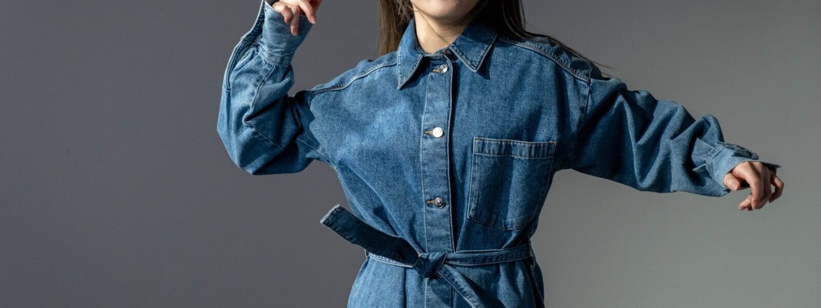 A fashionable woman poses confidently in a denim dress, showcasing modern style.