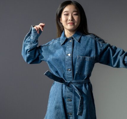 A fashionable woman poses confidently in a denim dress, showcasing modern style.