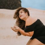 Woman in a black dress at the beach enjoying sand. Perfect for summer and leisure themes.