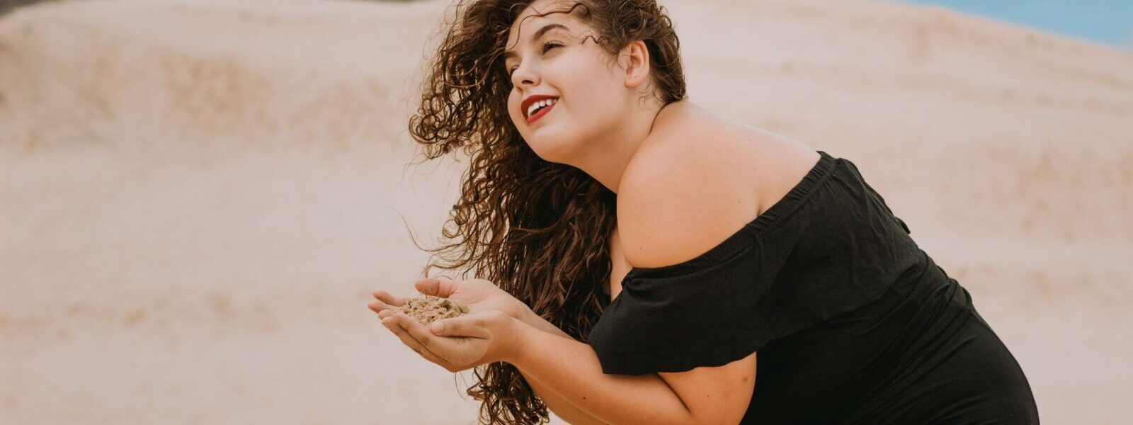 Woman in a black dress at the beach enjoying sand. Perfect for summer and leisure themes.
