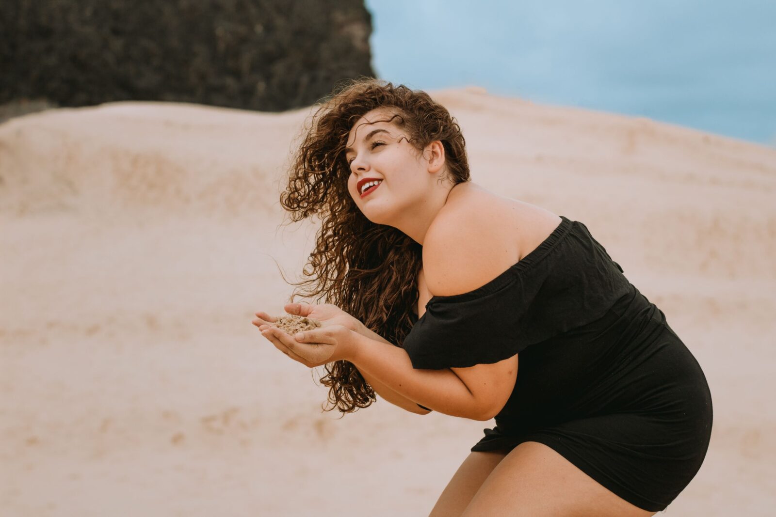 Woman in a black dress at the beach enjoying sand. Perfect for summer and leisure themes.